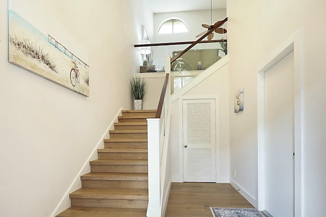 staircase featuring a high ceiling, baseboards, and wood finished floors