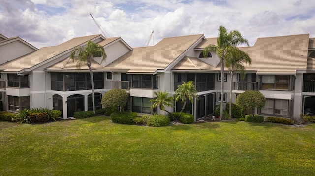 back of property with a sunroom, a tile roof, and a lawn