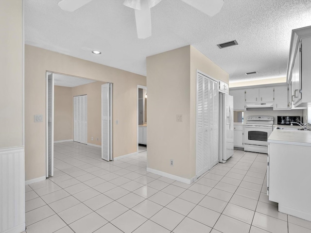 kitchen featuring white appliances, visible vents, light tile patterned flooring, light countertops, and under cabinet range hood