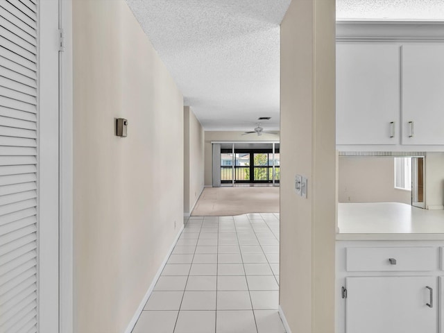 hall featuring light tile patterned floors, baseboards, and a textured ceiling