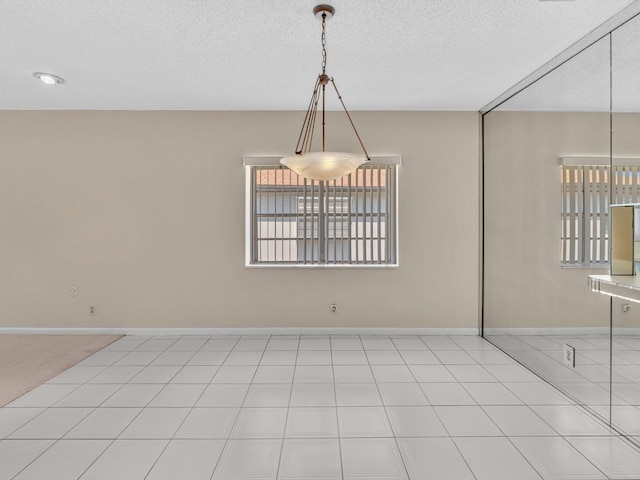 unfurnished dining area with light tile patterned flooring, a textured ceiling, and baseboards