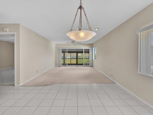 spare room featuring a textured ceiling, light tile patterned flooring, baseboards, and light carpet