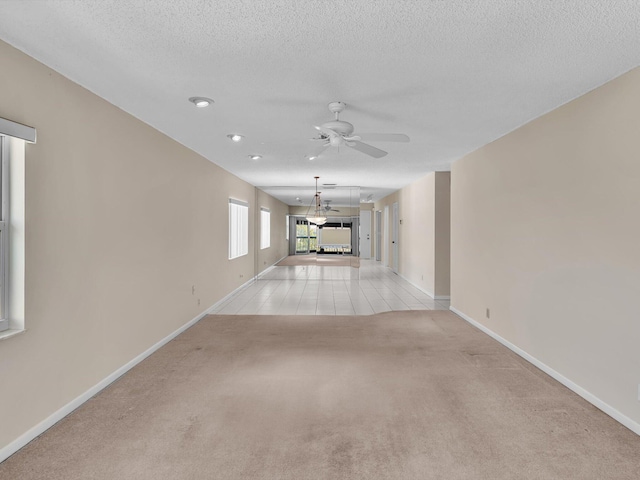 unfurnished living room with ceiling fan, a textured ceiling, baseboards, and light carpet