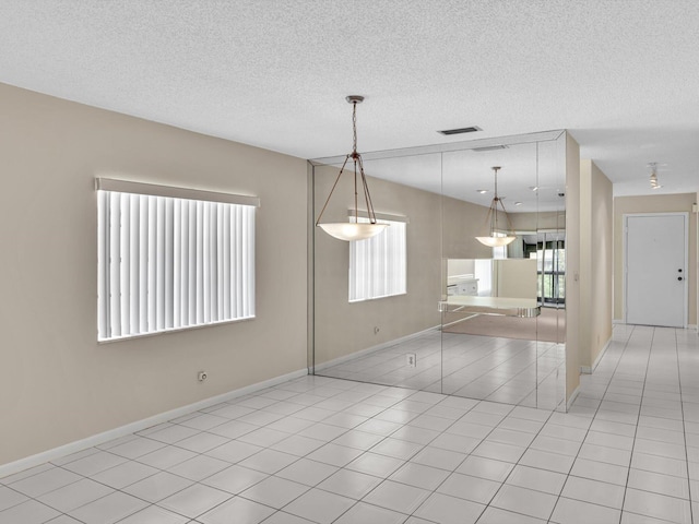 unfurnished dining area featuring light tile patterned floors, baseboards, and a textured ceiling