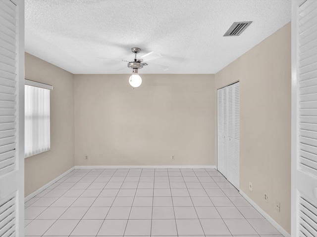 empty room with light tile patterned floors, a ceiling fan, visible vents, and baseboards