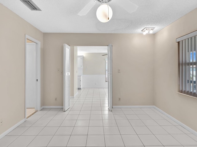 empty room with visible vents, a textured ceiling, light tile patterned floors, baseboards, and ceiling fan