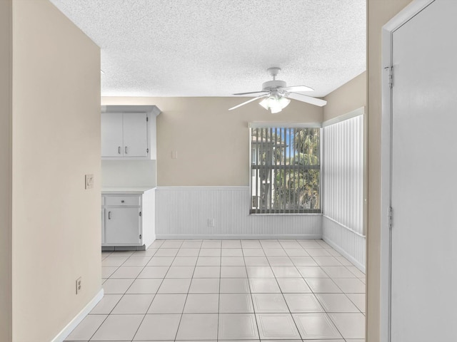 spare room with light tile patterned floors, a ceiling fan, wainscoting, and a textured ceiling