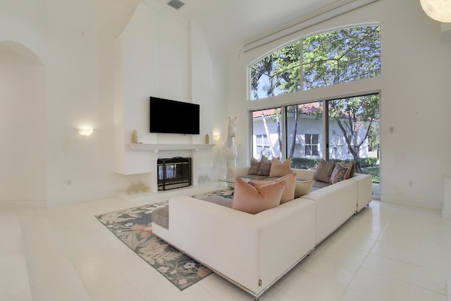 living area featuring light tile patterned floors, baseboards, arched walkways, a towering ceiling, and a premium fireplace