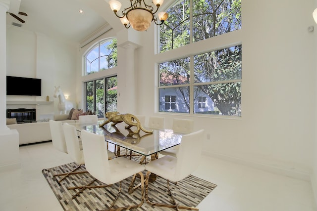 tiled dining area featuring decorative columns, visible vents, a high ceiling, an inviting chandelier, and a glass covered fireplace