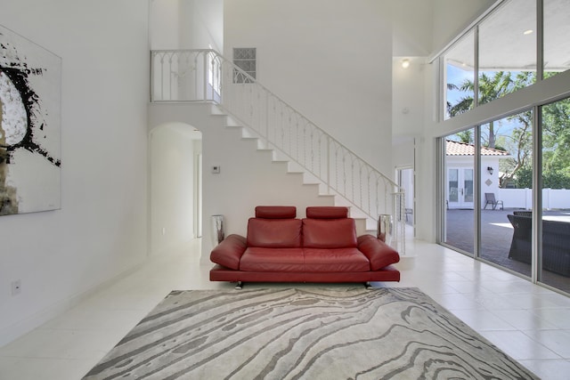 living area with a towering ceiling, stairway, arched walkways, and tile patterned floors