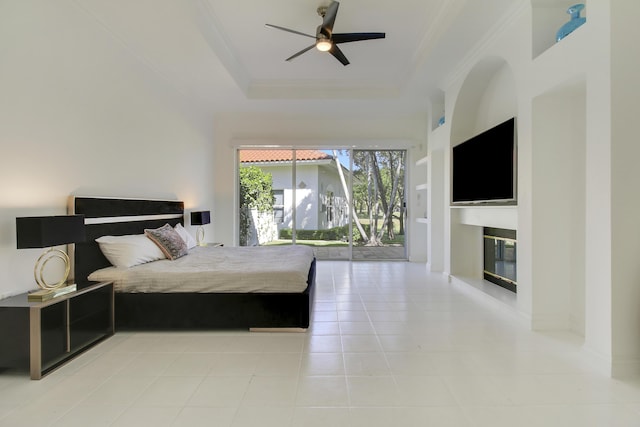 bedroom with access to exterior, a raised ceiling, ornamental molding, a glass covered fireplace, and tile patterned floors