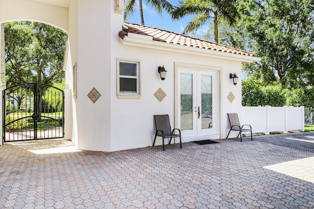 property entrance with stucco siding, a tiled roof, fence, and french doors