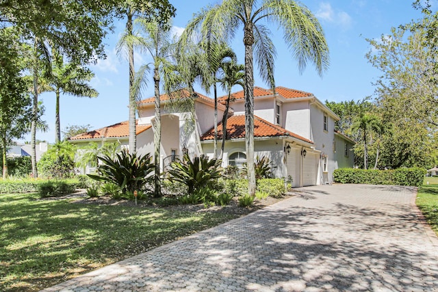 view of side of property featuring a garage, a tiled roof, decorative driveway, a lawn, and stucco siding