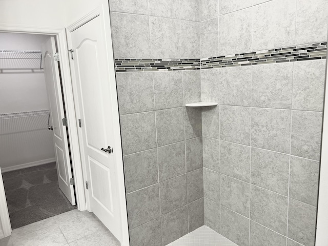 bathroom with wainscoting, tile patterned flooring, a tile shower, and a walk in closet