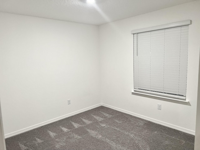 unfurnished room featuring baseboards and dark colored carpet