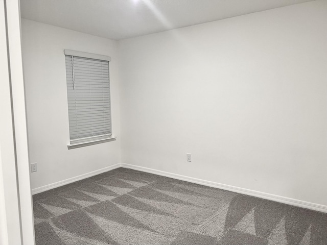 empty room featuring baseboards and dark colored carpet