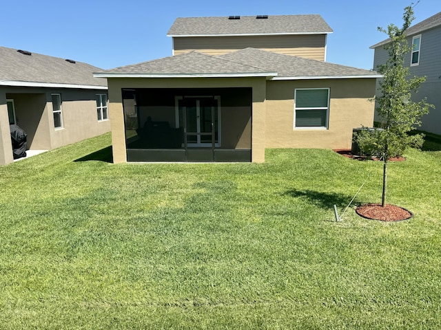 back of property featuring a sunroom, roof with shingles, a yard, and stucco siding