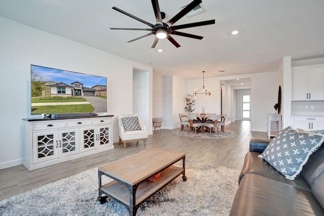 living room with ceiling fan with notable chandelier, light wood-style flooring, recessed lighting, and baseboards