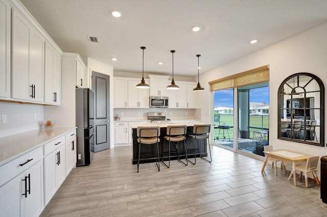 kitchen with visible vents, appliances with stainless steel finishes, a breakfast bar area, white cabinets, and light countertops