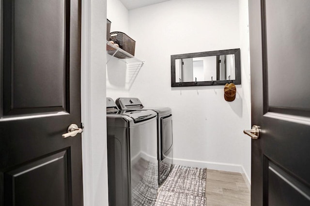 washroom with light wood finished floors, laundry area, washer and dryer, and baseboards