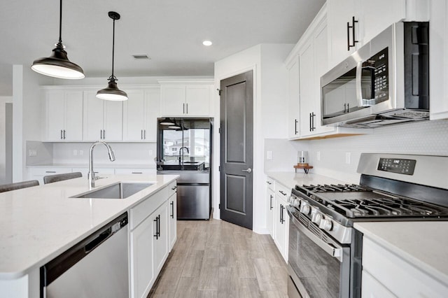 kitchen featuring a sink, white cabinets, appliances with stainless steel finishes, decorative light fixtures, and light wood-type flooring