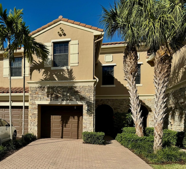 mediterranean / spanish house with a garage, a tile roof, stone siding, decorative driveway, and stucco siding