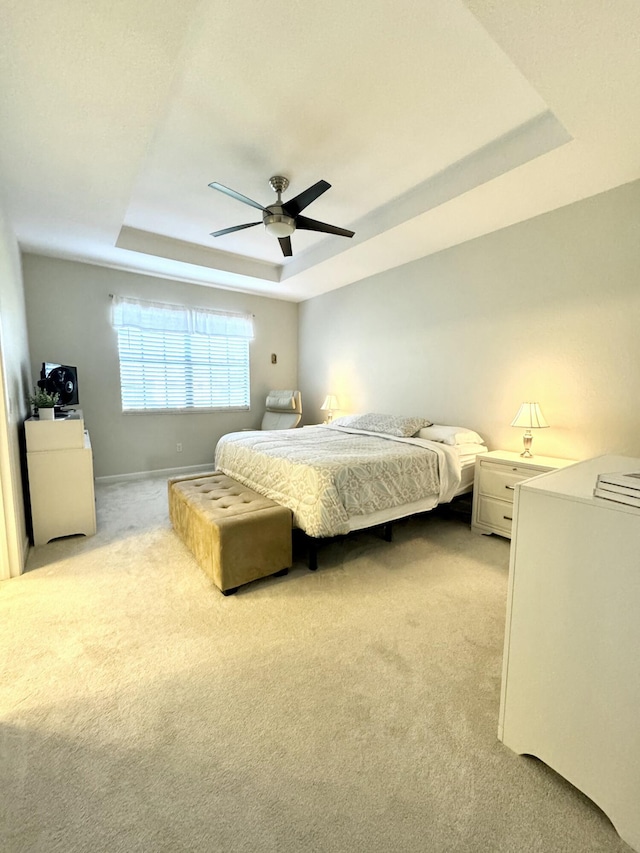 bedroom featuring baseboards, a tray ceiling, a ceiling fan, and light colored carpet