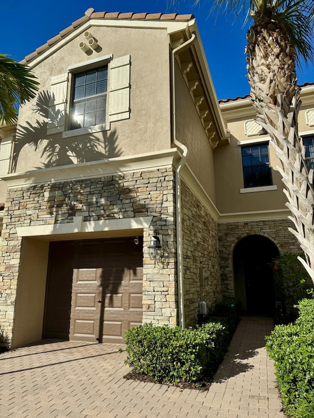 view of front facade featuring stone siding, a tiled roof, an attached garage, and stucco siding