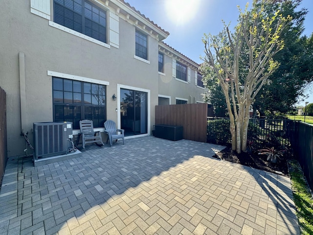 rear view of property with a patio, stucco siding, central AC, a fenced backyard, and a tiled roof