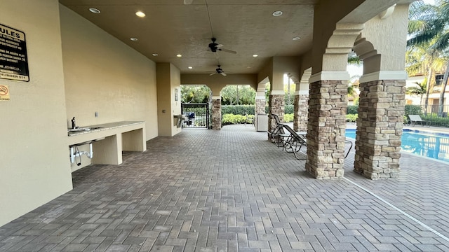 view of patio / terrace with ceiling fan, an outdoor kitchen, fence, and a community pool