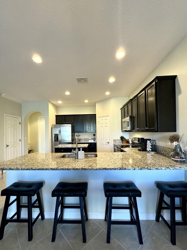 kitchen with arched walkways, a sink, visible vents, stainless steel fridge with ice dispenser, and light stone countertops