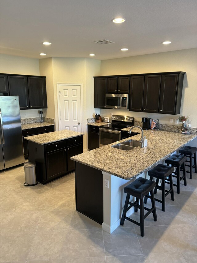 kitchen with light stone counters, arched walkways, stainless steel appliances, visible vents, and a sink