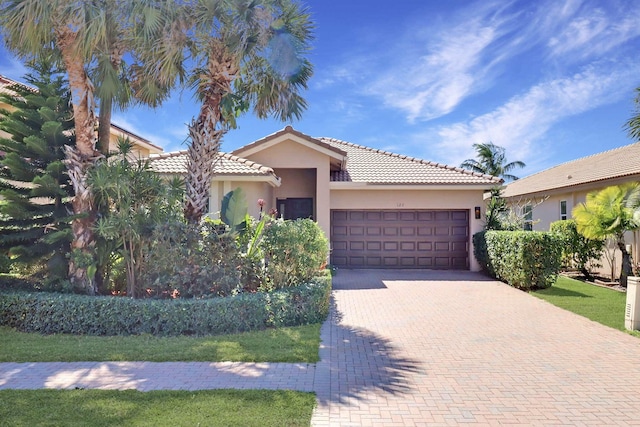 view of front of home with decorative driveway, a tile roof, an attached garage, and stucco siding