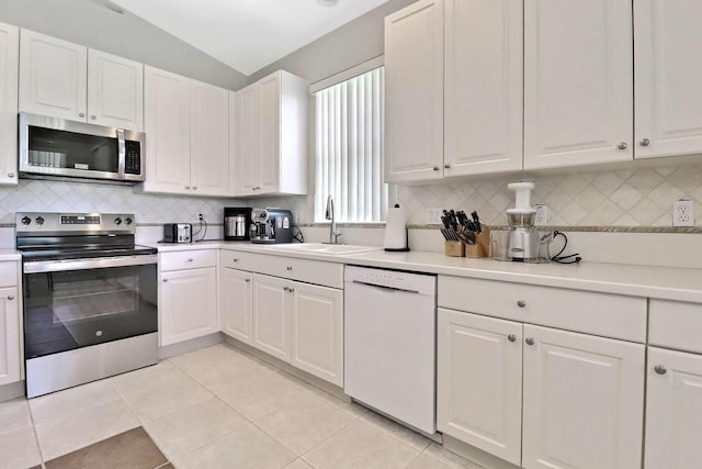 kitchen with a sink, light countertops, vaulted ceiling, appliances with stainless steel finishes, and white cabinetry