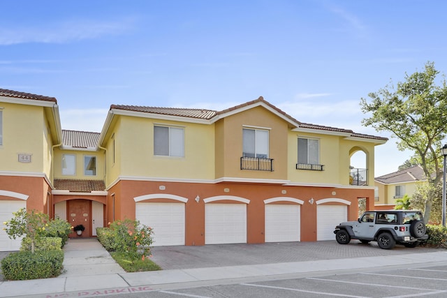 view of front of property with a tile roof, an attached garage, driveway, and stucco siding