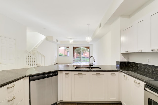 kitchen with dark stone counters, a peninsula, stainless steel appliances, white cabinetry, and a sink