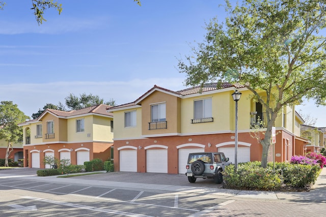 townhome / multi-family property with stucco siding, driveway, a tile roof, a residential view, and a garage