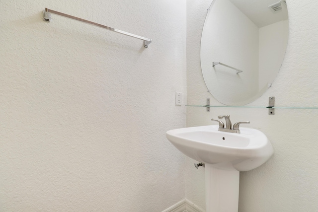 bathroom featuring a textured wall, visible vents, and a sink