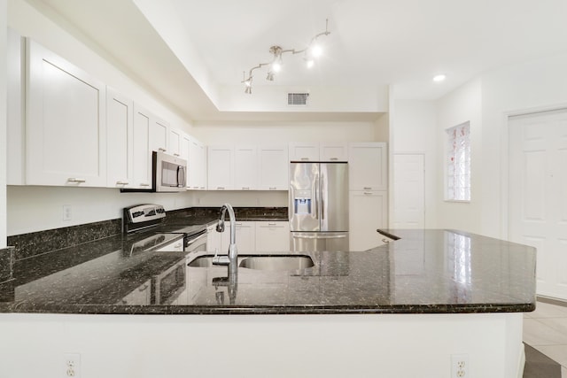 kitchen featuring visible vents, dark stone counters, a peninsula, a sink, and stainless steel appliances