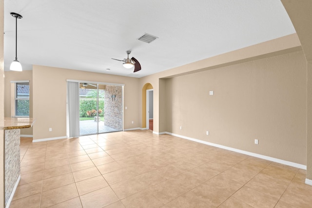 unfurnished room with arched walkways, light tile patterned floors, baseboards, and ceiling fan