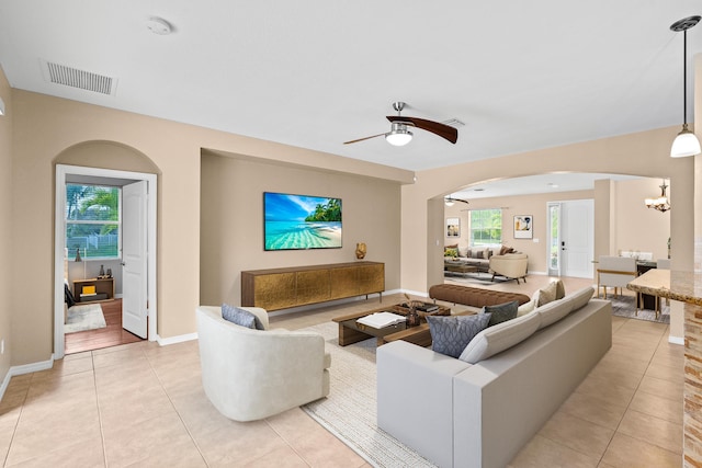 living area featuring visible vents, ceiling fan with notable chandelier, arched walkways, light tile patterned floors, and baseboards