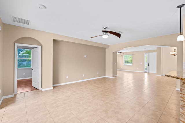 unfurnished living room with visible vents, baseboards, ceiling fan with notable chandelier, arched walkways, and light tile patterned flooring