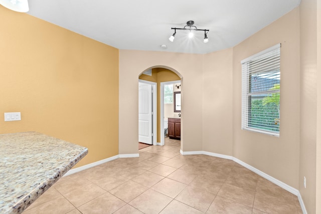 spare room featuring arched walkways, light tile patterned floors, rail lighting, and baseboards