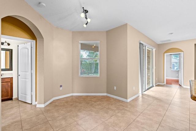 empty room with arched walkways, plenty of natural light, baseboards, and light tile patterned flooring