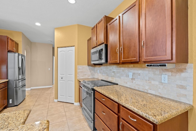 kitchen featuring brown cabinetry, light stone counters, decorative backsplash, light tile patterned flooring, and stainless steel appliances