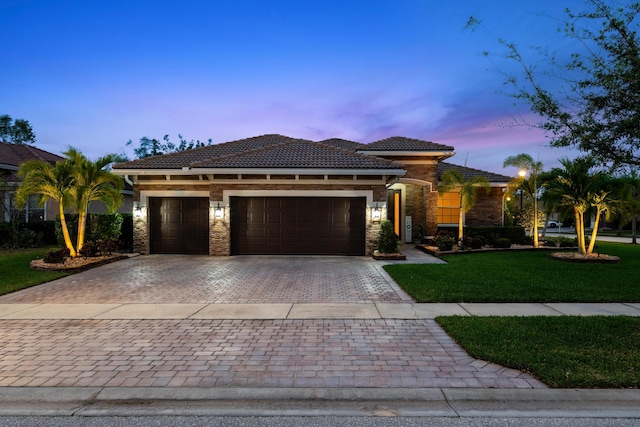 view of front of house featuring a tile roof, decorative driveway, stone siding, and a front lawn