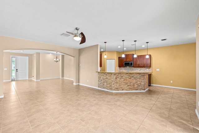 unfurnished living room with visible vents, baseboards, ceiling fan, light tile patterned floors, and arched walkways