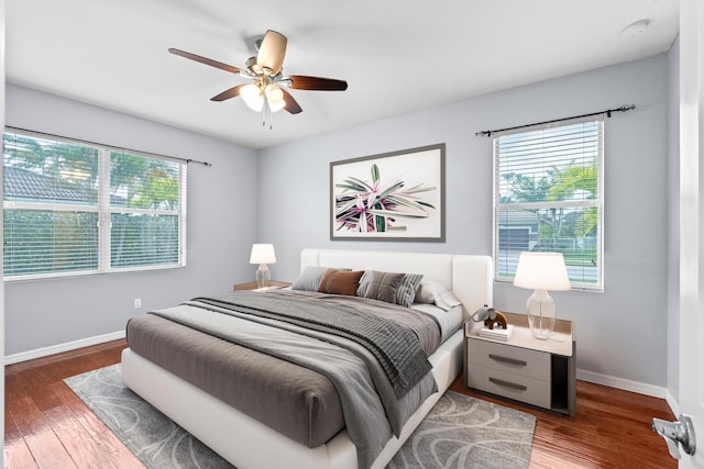 bedroom featuring ceiling fan, baseboards, multiple windows, and wood finished floors