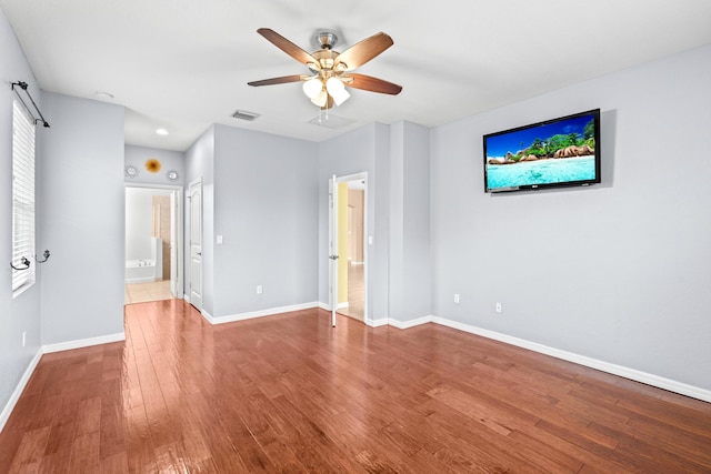 interior space with visible vents, a ceiling fan, ensuite bathroom, wood finished floors, and baseboards