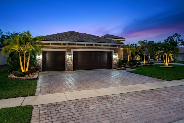 view of front of house featuring a front yard, an attached garage, stone siding, a tiled roof, and decorative driveway